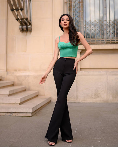 Woman in a green top and black pants standing in front of a building.