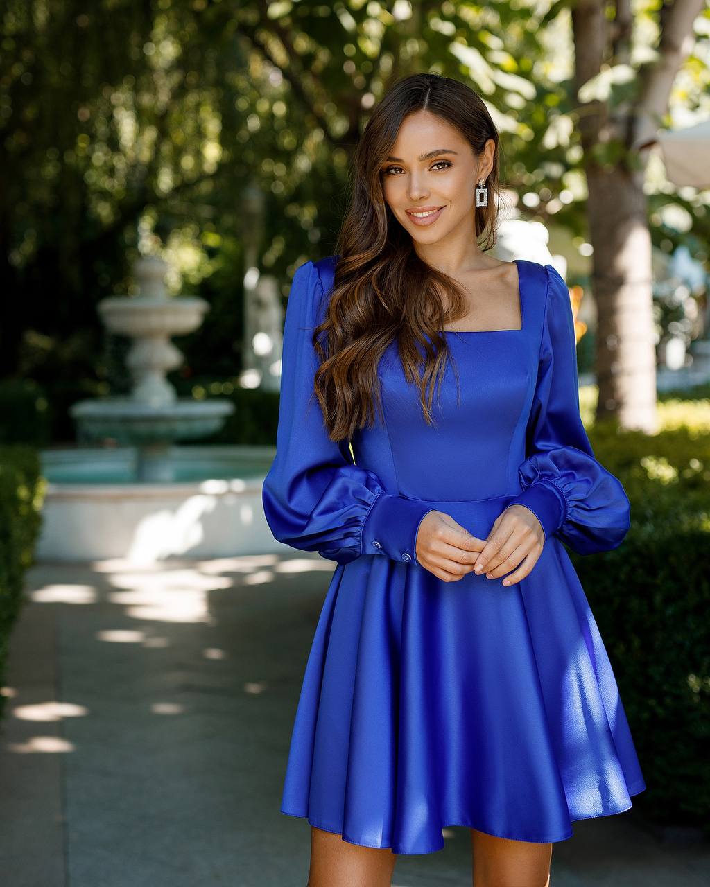 Woman wearing a blue dress standing outdoors with trees in the background
