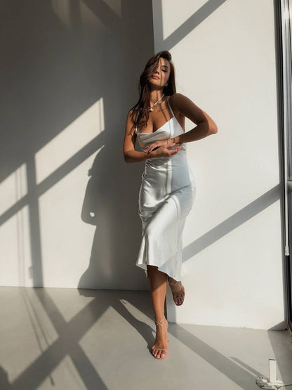 Woman in a silver dress standing against a white wall with shadows.