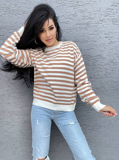 Woman wearing a striped sweater and jeans against a gray wall