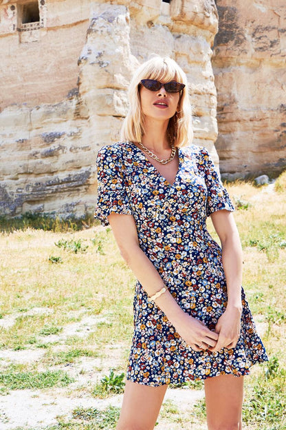 Woman in a floral dress standing in front of a stone wall.