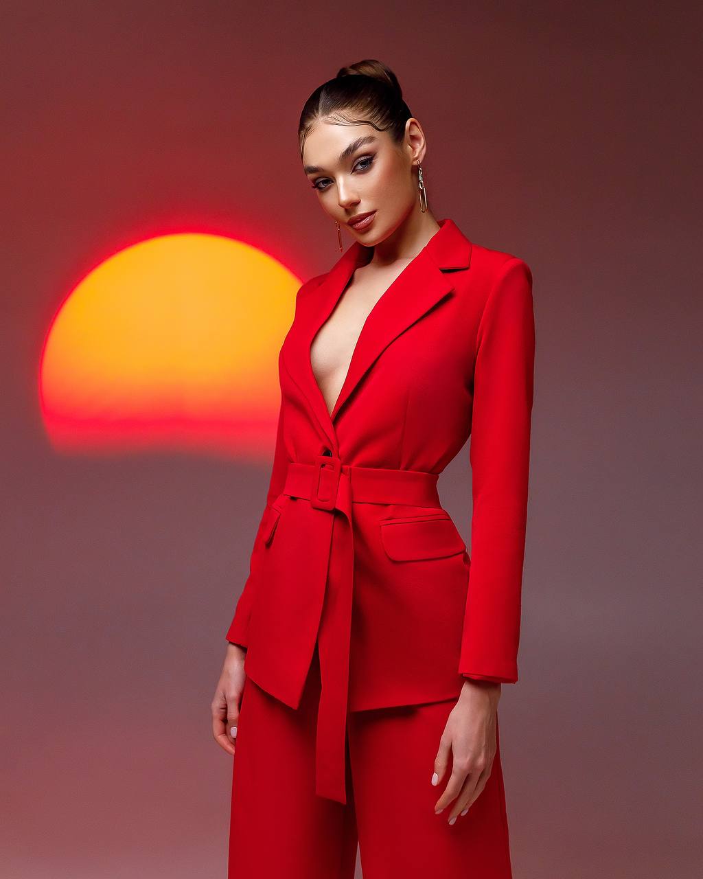 Woman in a red suit standing against a sunset background
