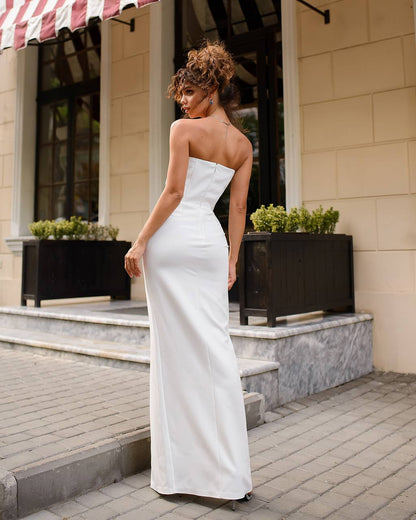 Woman in a white strapless gown standing on a sidewalk with a building in the background
