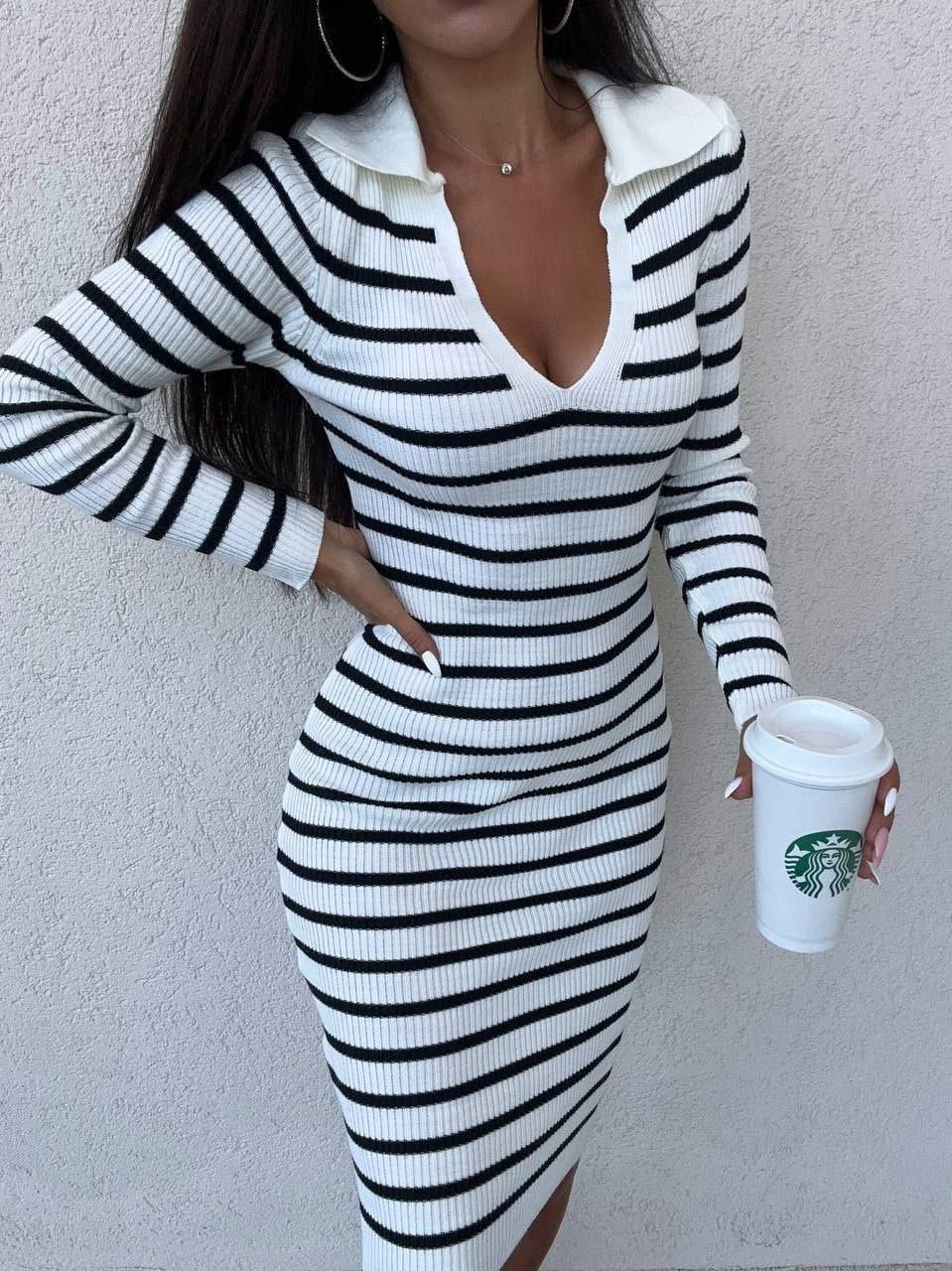 Person wearing a black and white striped dress holding a Starbucks cup against a plain background