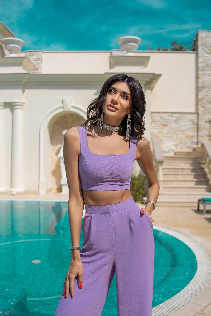 Woman in a purple outfit standing by a pool with classical architecture in the background