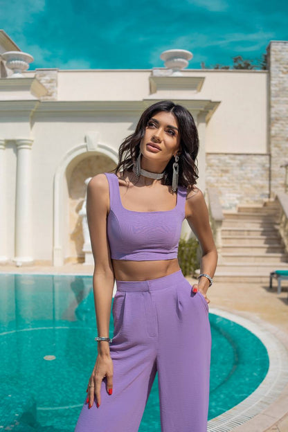 Woman in a purple outfit standing by a pool with classical architecture in the background