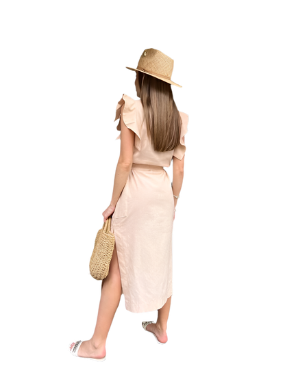 Woman wearing a beige dress and hat, holding a straw bag on a white background