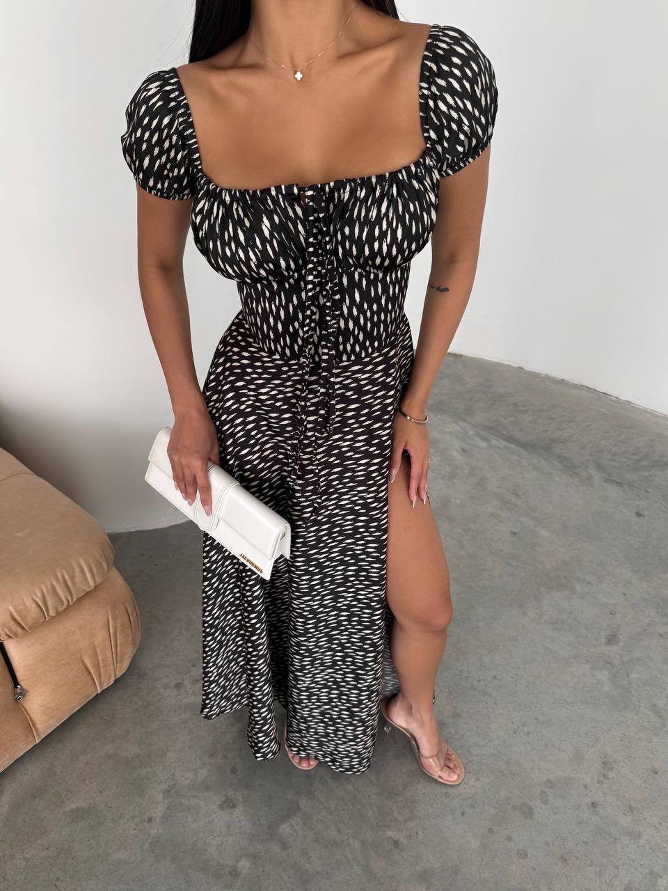 Woman wearing a black and white patterned dress with a slit, holding a clutch.