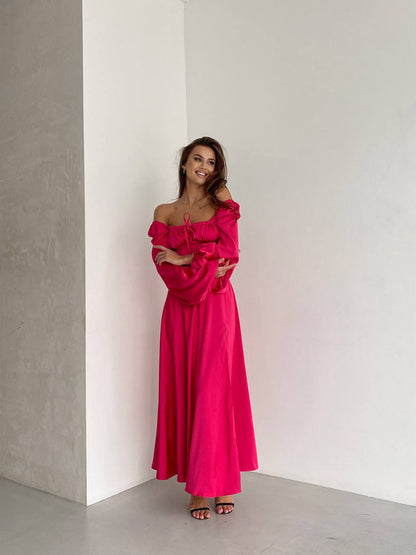 Woman wearing a bright pink off-shoulder dress against a plain white wall.