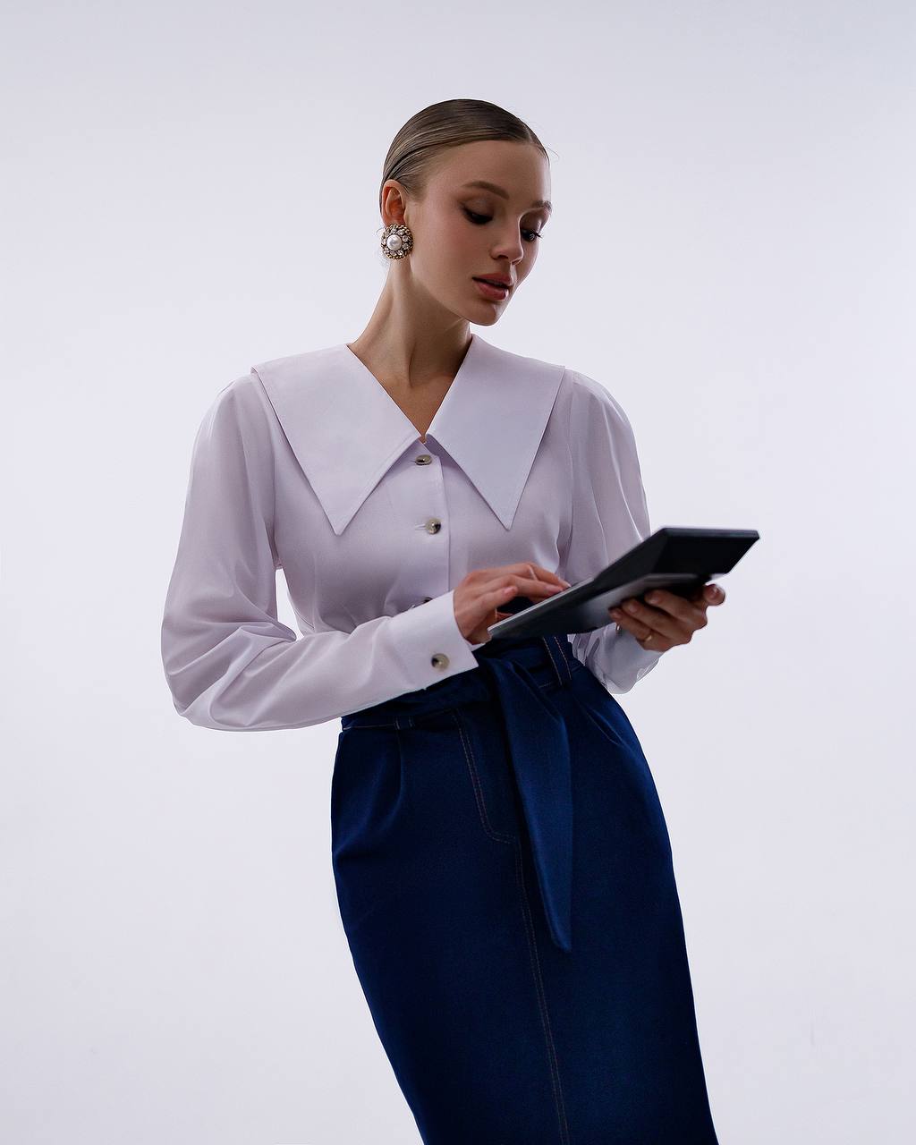 Woman in a white blouse and blue skirt using a tablet on a plain background
