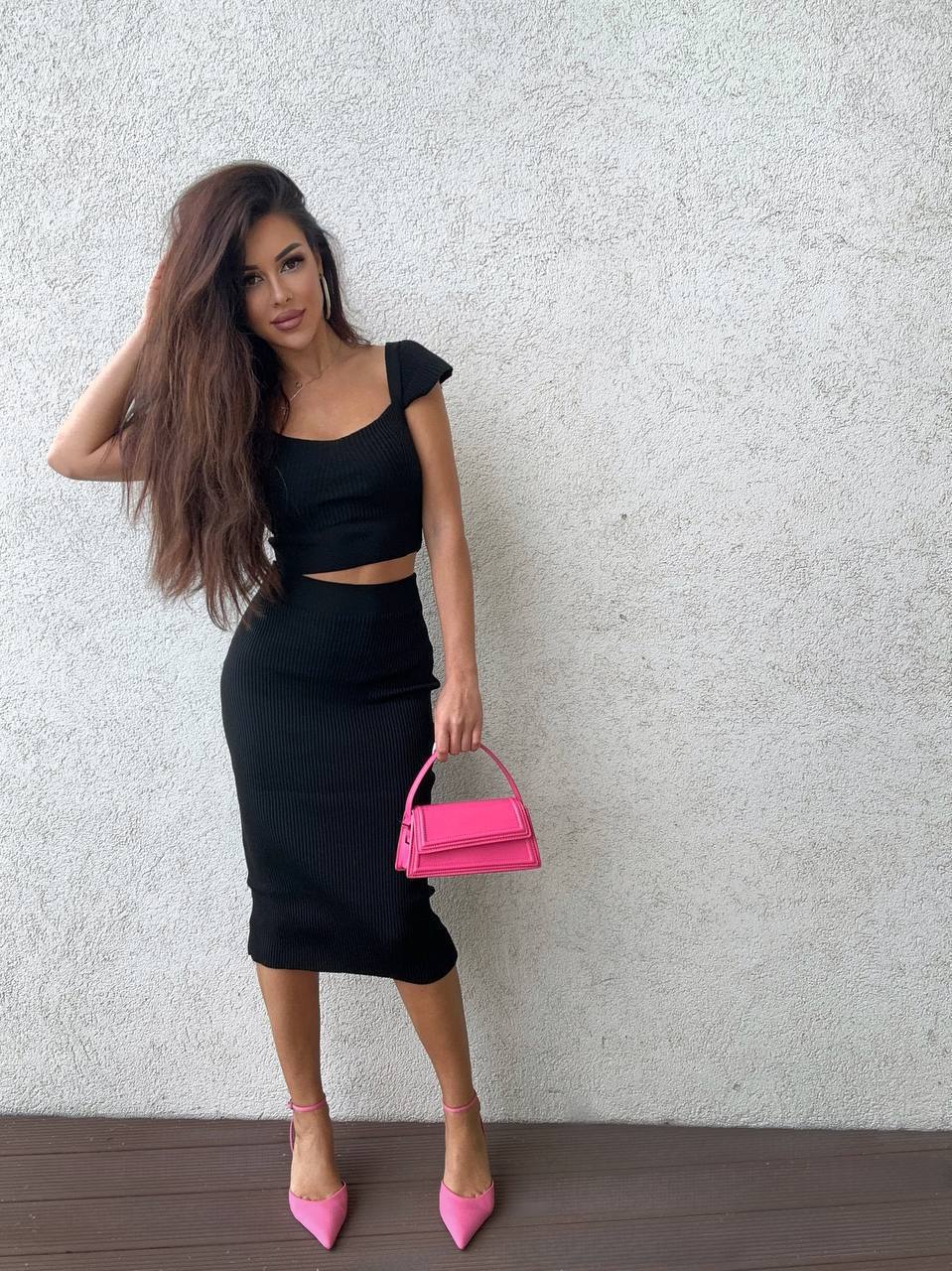 Woman in black outfit holding a pink handbag against a light gray background