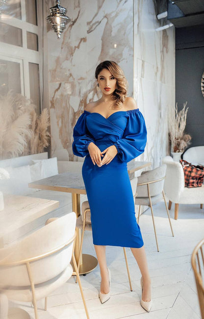 Woman in a blue off-shoulder dress standing in a modern interior setting.