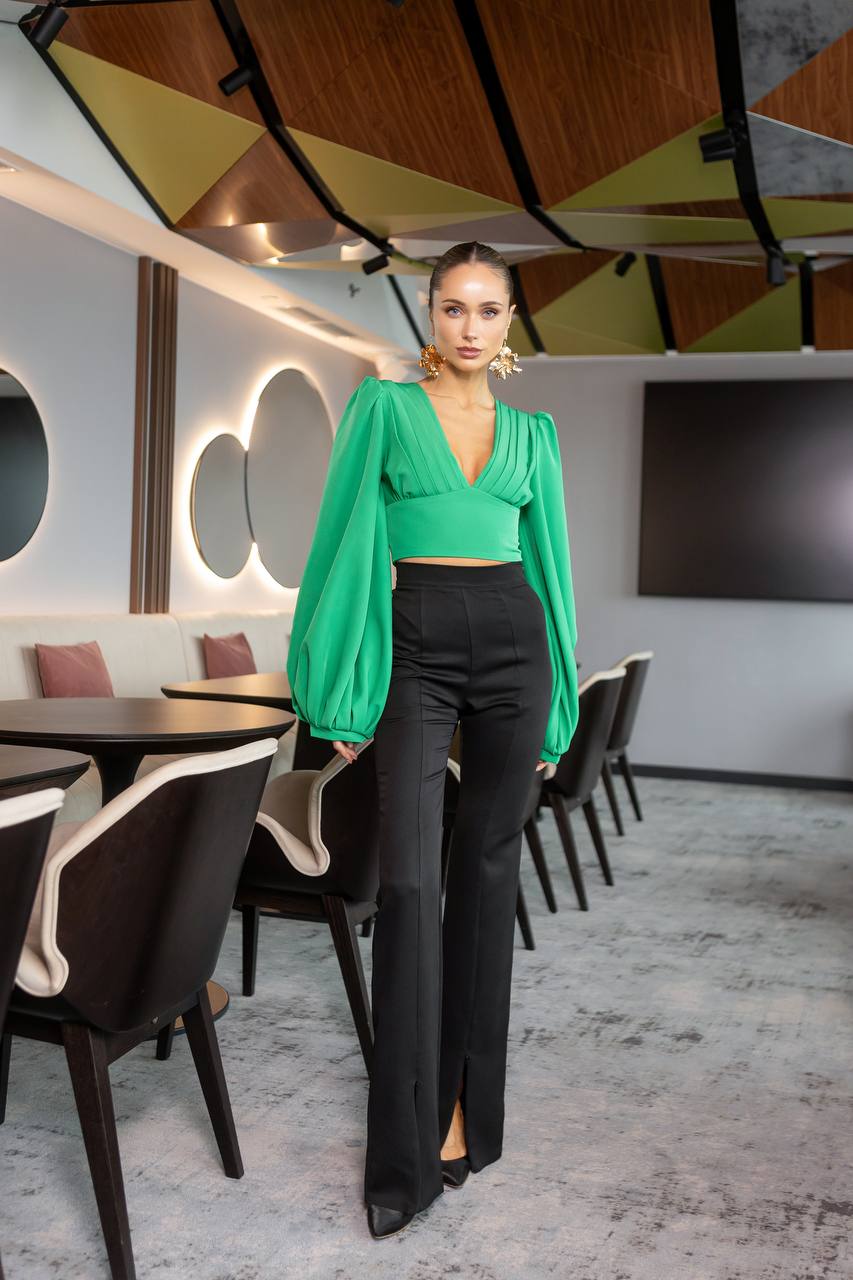 Woman in a green top and black pants standing in a modern restaurant setting.