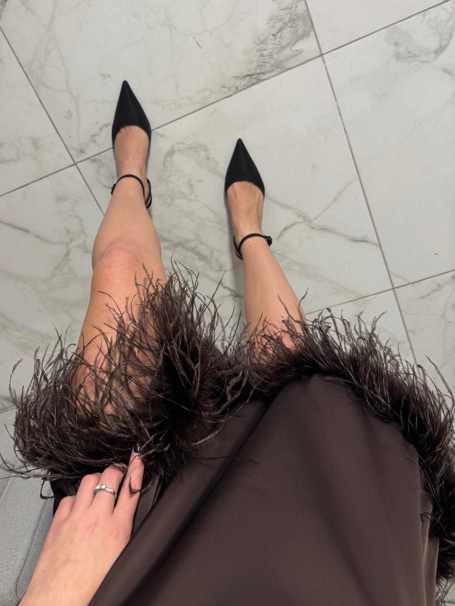 Person wearing black high-heeled shoes with feathered skirt on marble floor