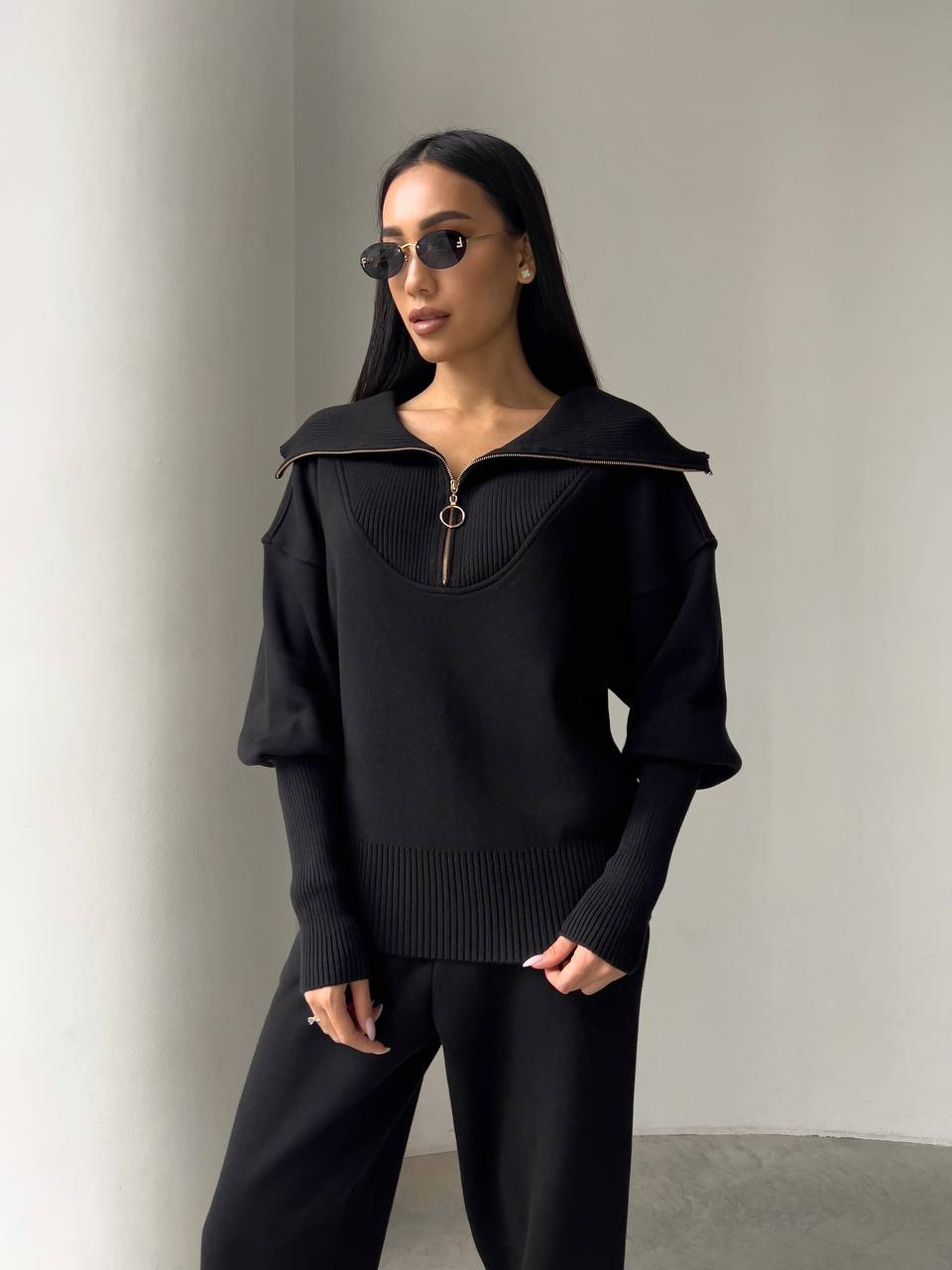 Woman wearing a black outfit with a high collar against a neutral background