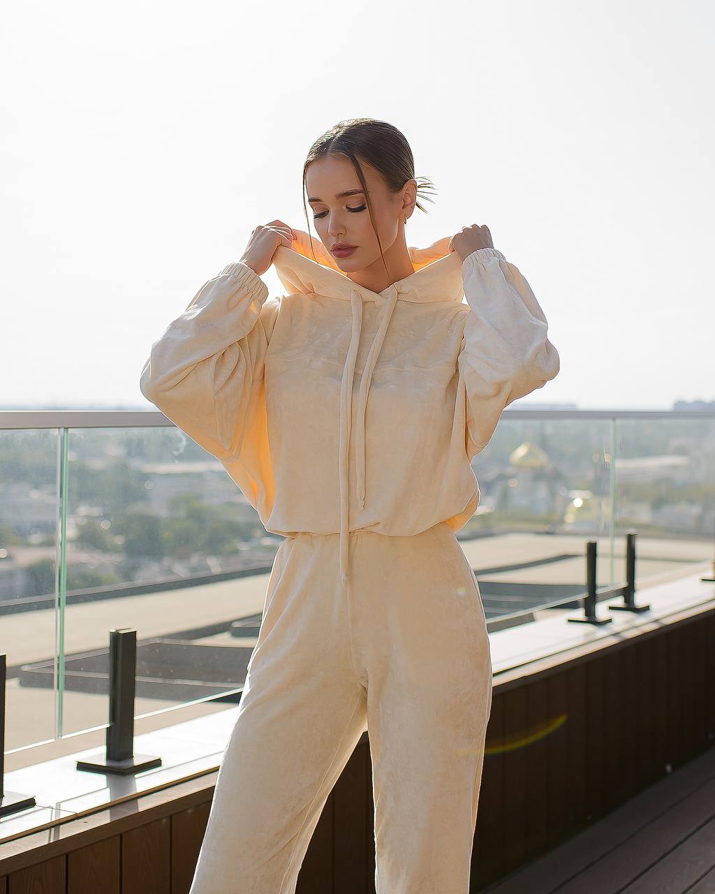 Woman in a beige tracksuit standing on a balcony with a cityscape background