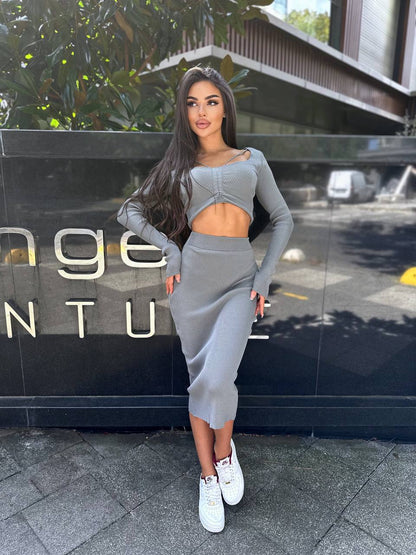 Woman in a gray outfit standing in front of a building entrance.