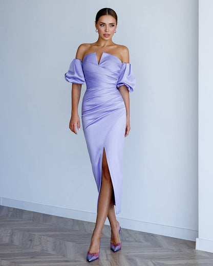Woman wearing a lavender off-shoulder dress with a high slit on a plain background