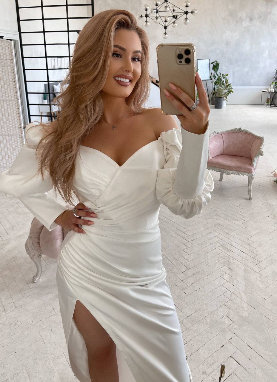 Woman taking a mirror selfie wearing a white dress with long sleeves in a stylish room.