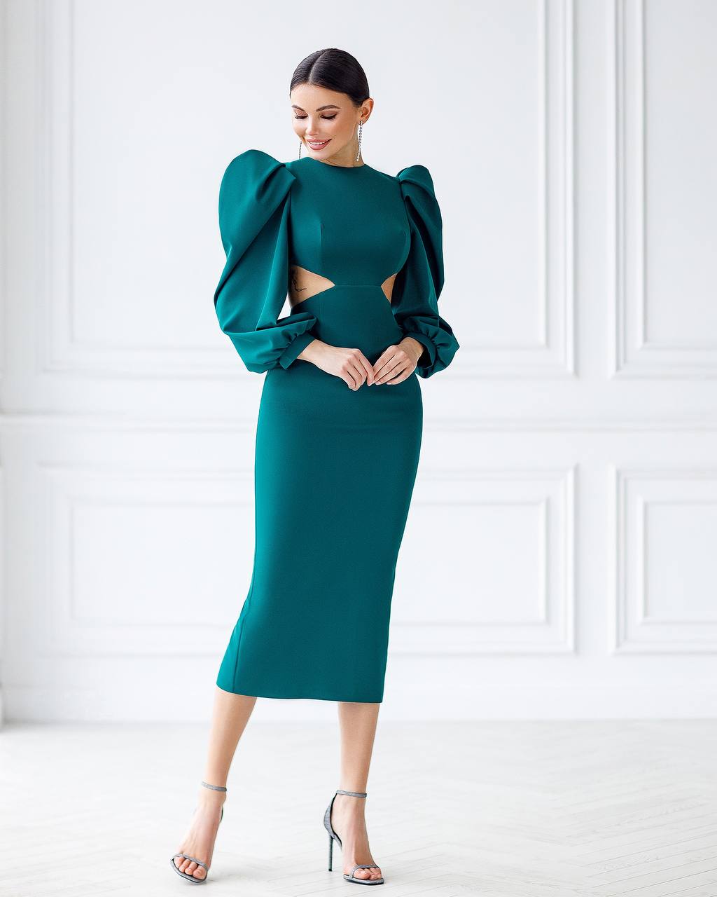 Woman wearing a teal dress with puffed sleeves against a white wall