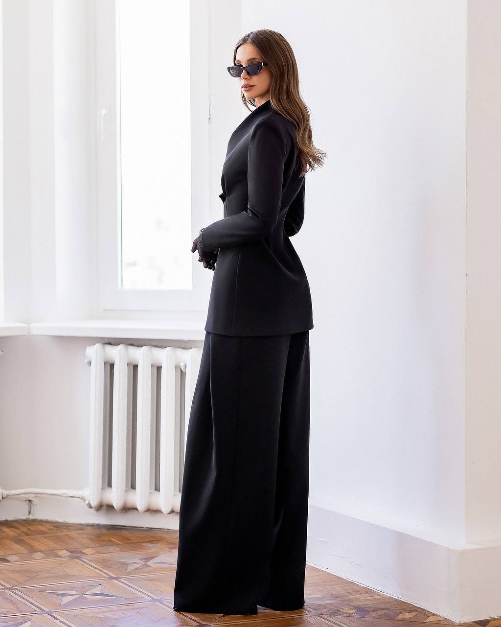 Woman wearing a black outfit standing in a room with white walls and a radiator.