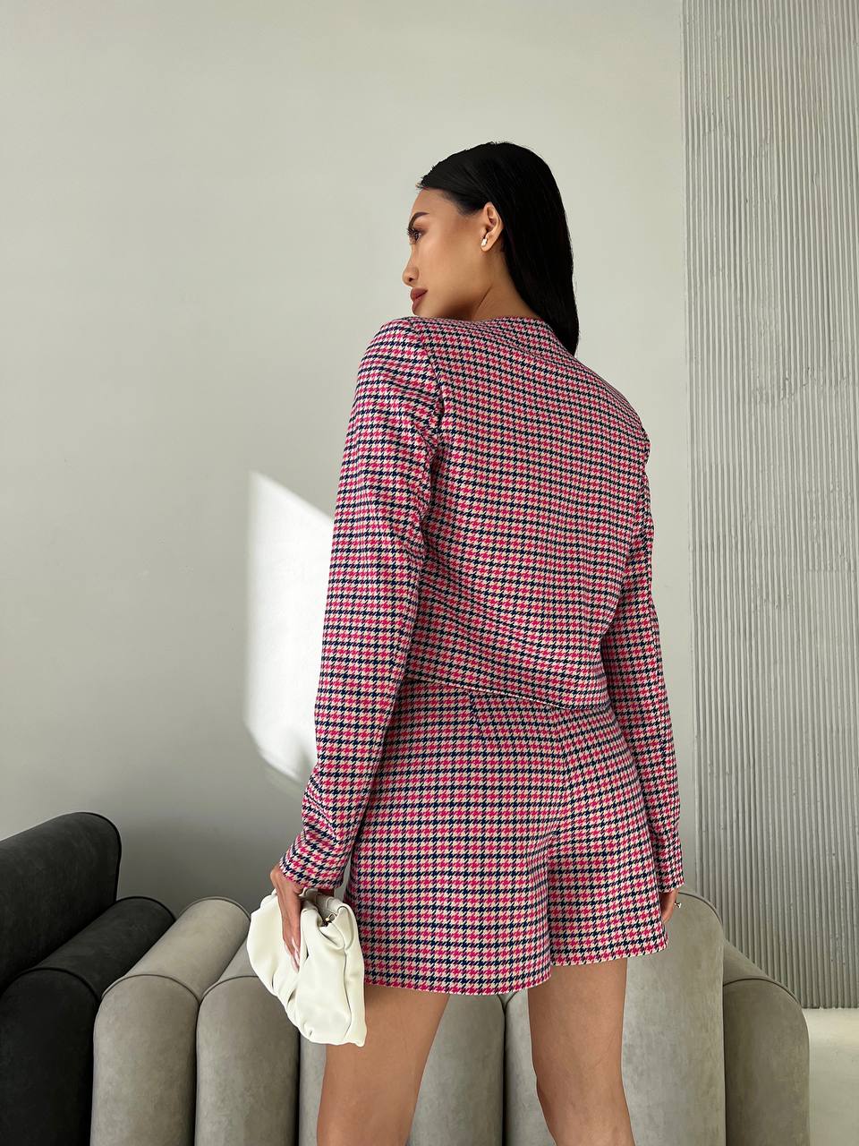 Woman wearing a red and black checkered suit standing in a room with a neutral color scheme.