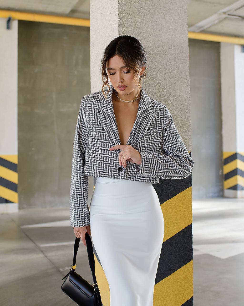 Woman in a checkered blazer and white skirt standing in an industrial setting.