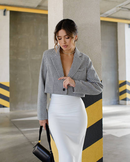 Woman in a checkered blazer and white skirt standing in an industrial setting.