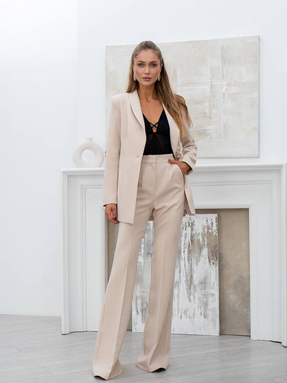 Woman in a beige suit standing in a modern interior setting with abstract art on the wall.