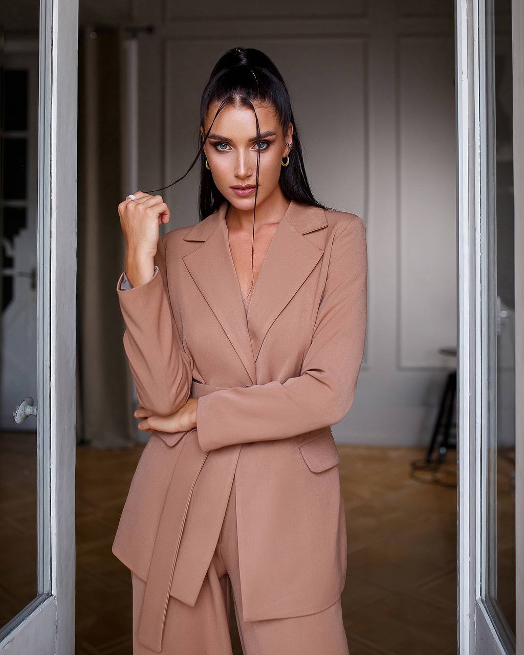 Woman in a beige suit standing in a doorway.