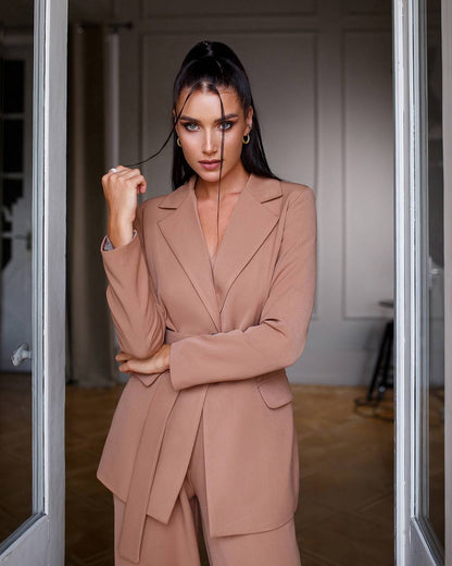 Woman in a beige suit standing in a doorway.