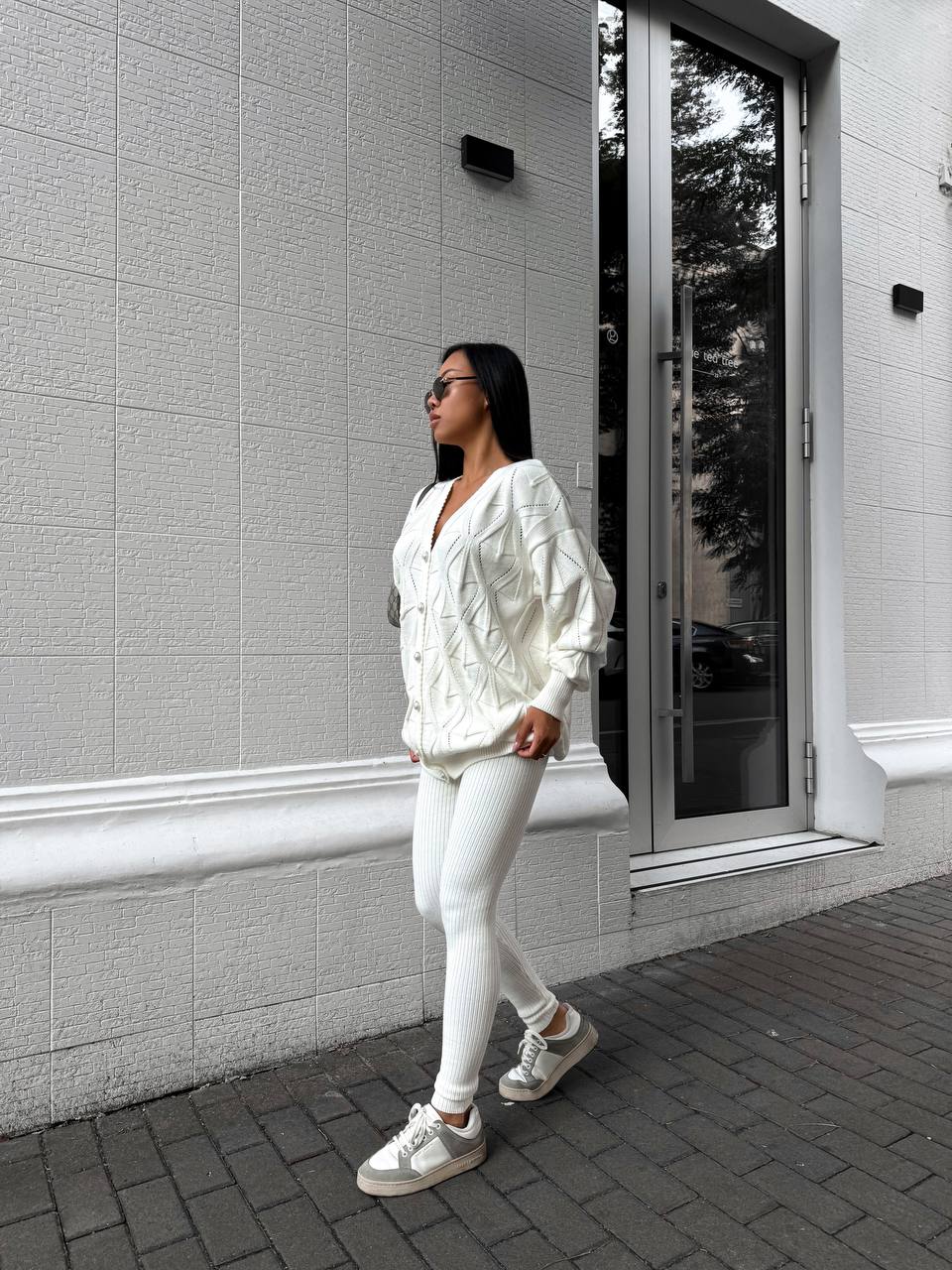 Person wearing a white outfit standing against a gray building.