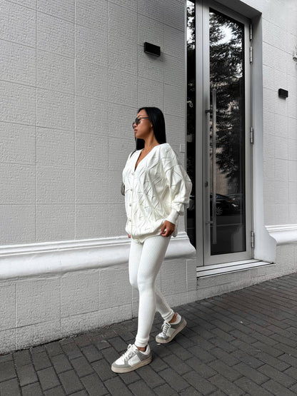 Person wearing a white outfit standing against a gray building.