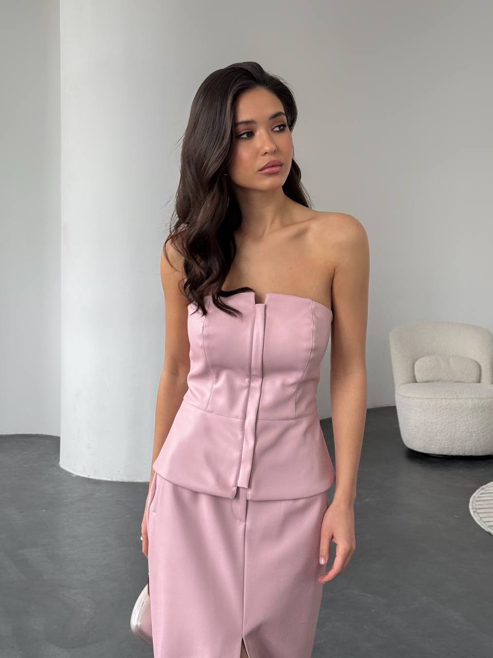 Woman wearing a pink strapless outfit in a minimalistic room.
