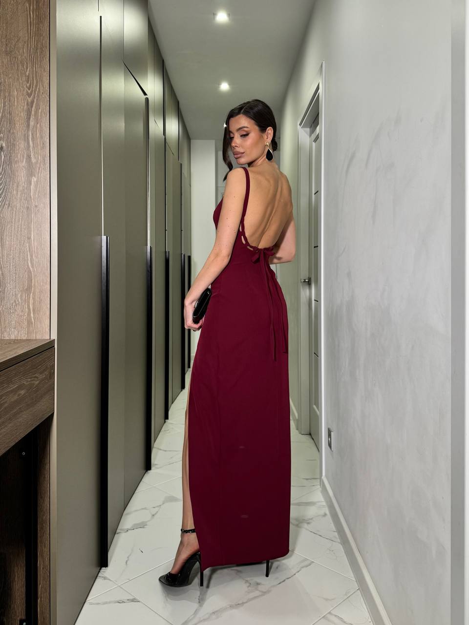 Woman in a burgundy dress standing in a modern hallway.