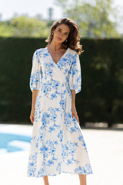 Woman wearing a white dress with blue floral patterns by a poolside.