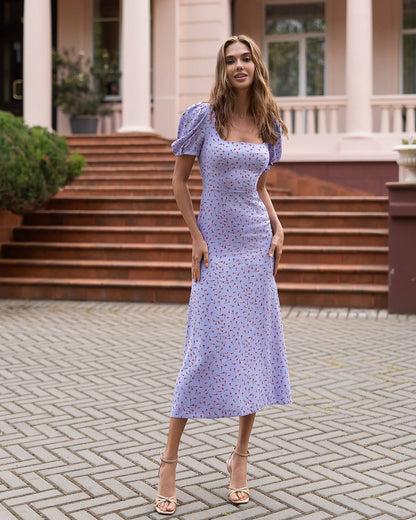 Woman in a light purple floral dress standing in front of steps.