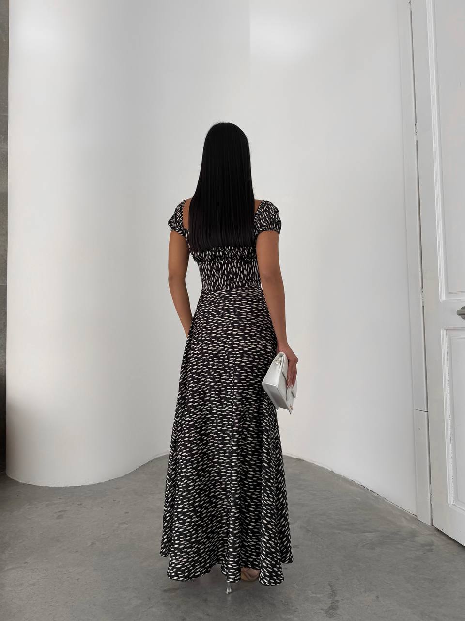 Woman in a black and white patterned dress standing in a minimalistic room.