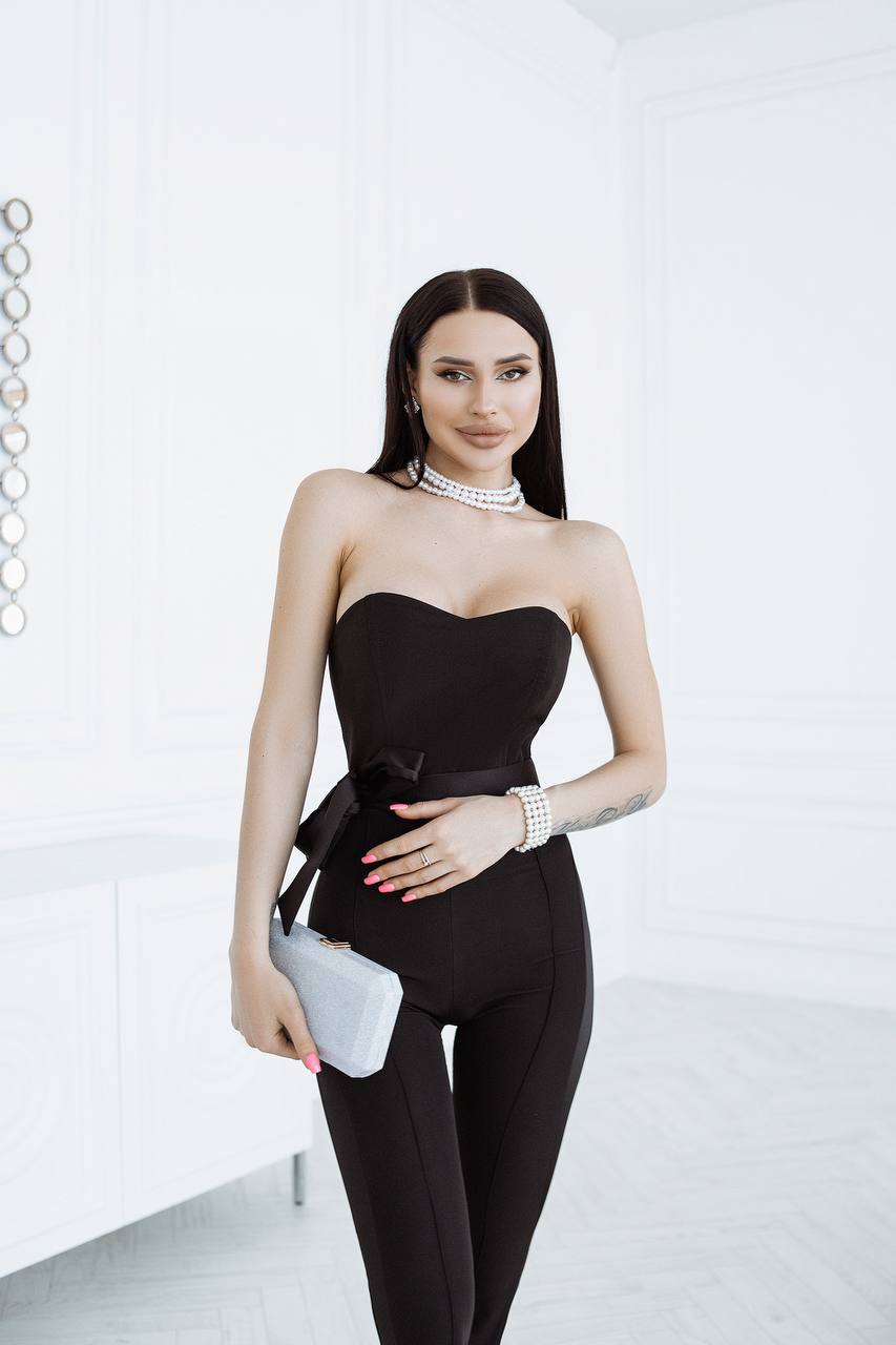 Woman in a black strapless outfit holding a clutch against a white background