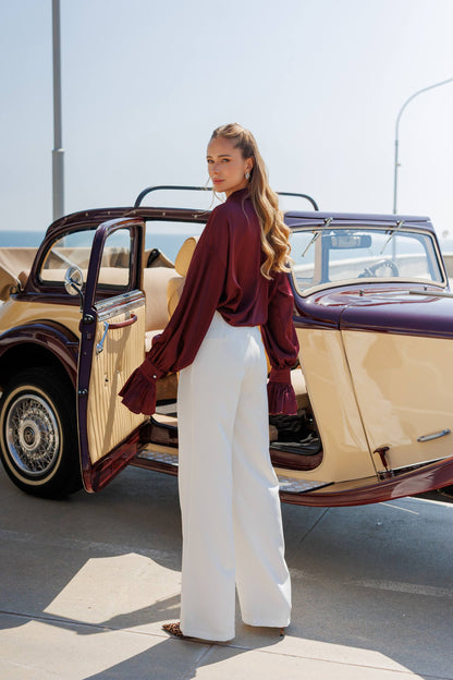 Woman standing next to a vintage car with an open door on a sunny day.