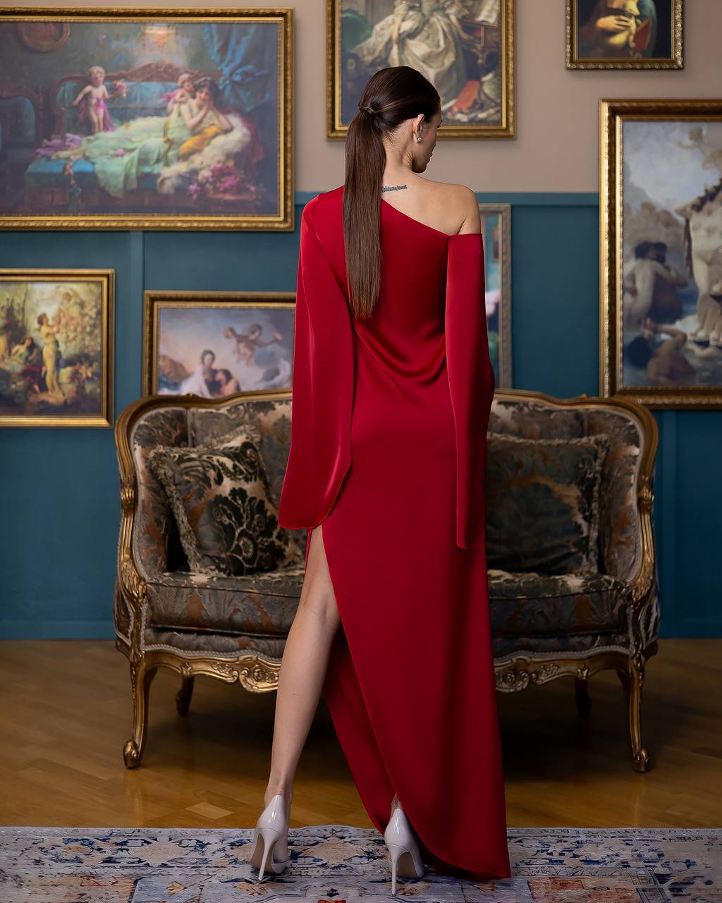 Woman in a red dress standing in an elegant room with classical paintings and furniture.