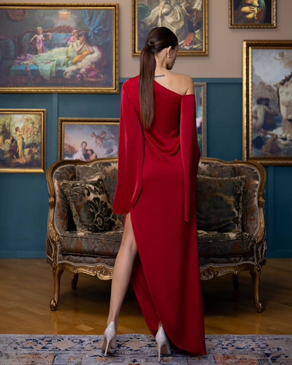 Woman in a red dress standing in an elegant room with classical paintings and furniture.