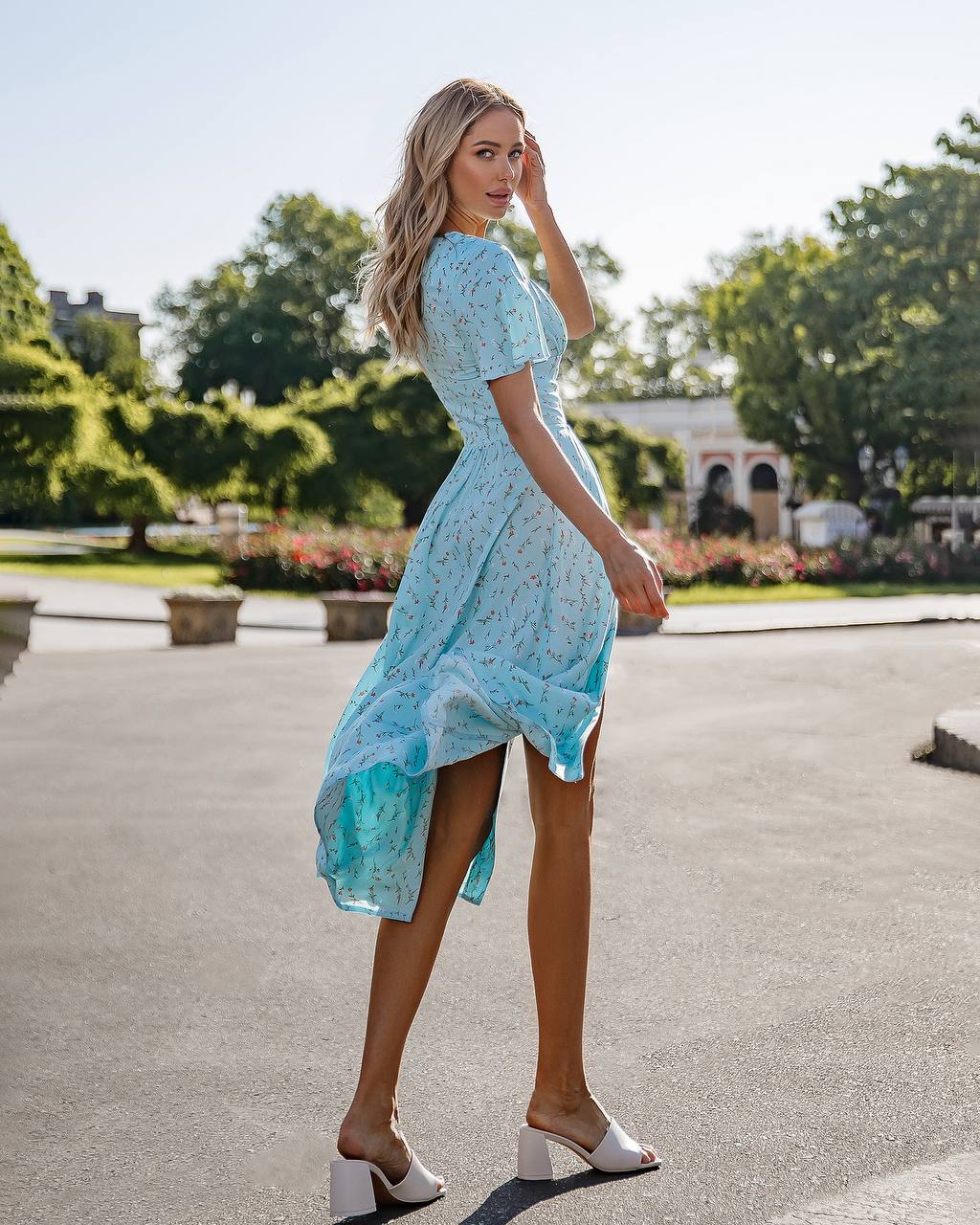 Woman in a light blue dress standing outdoors with greenery in the background