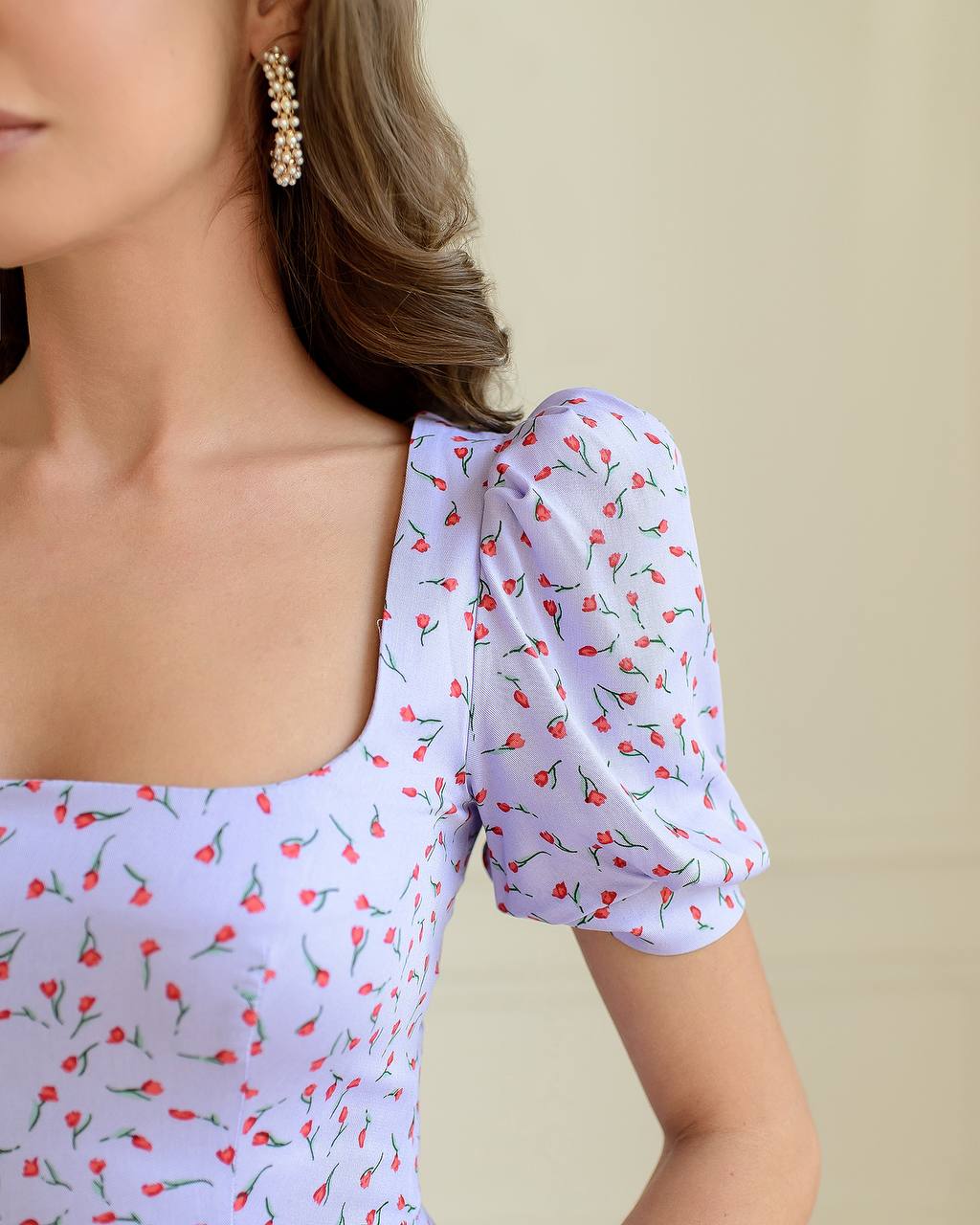 Woman wearing a light blue dress with red floral pattern on a beige background
