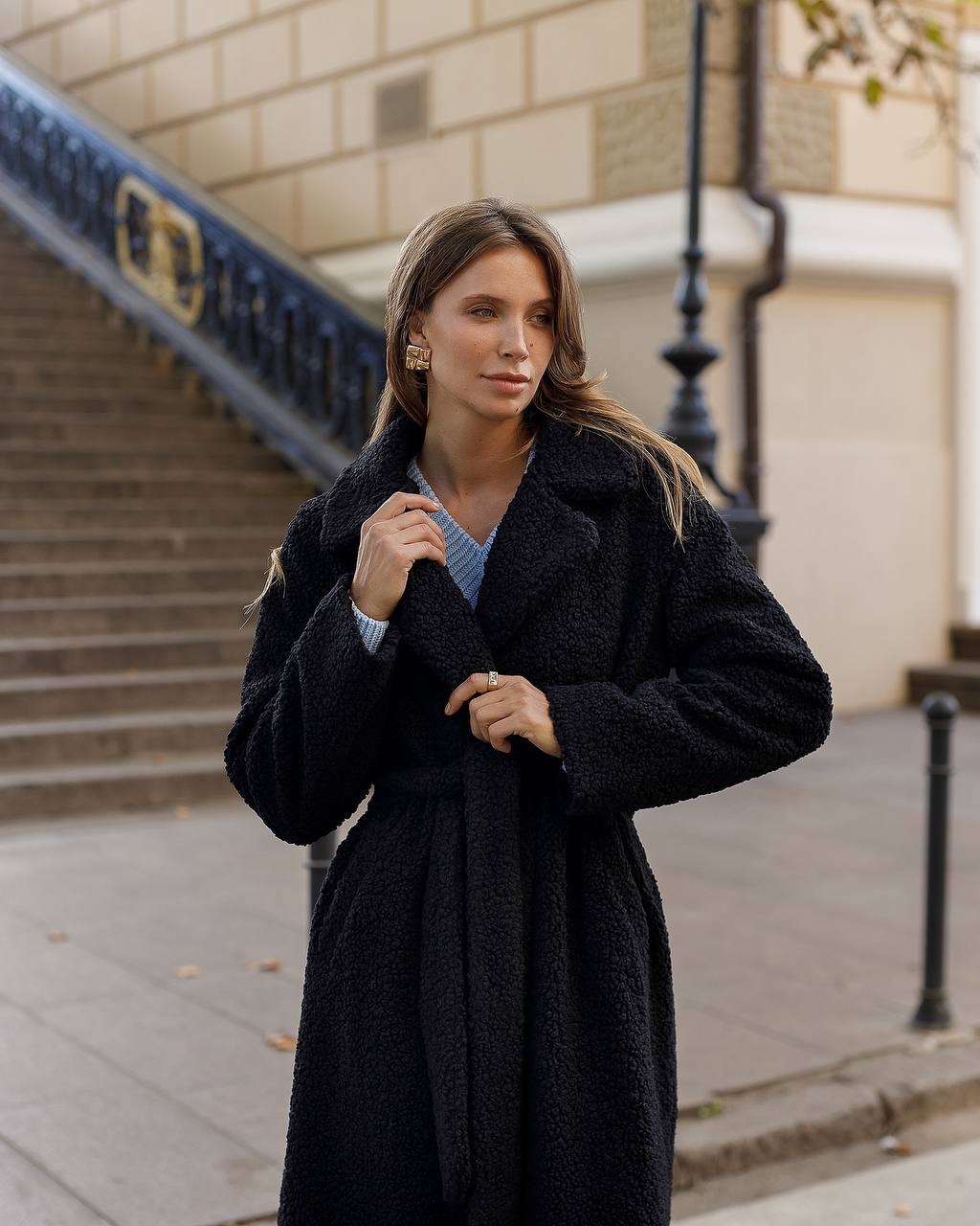 Woman wearing a black coat standing on a city street.