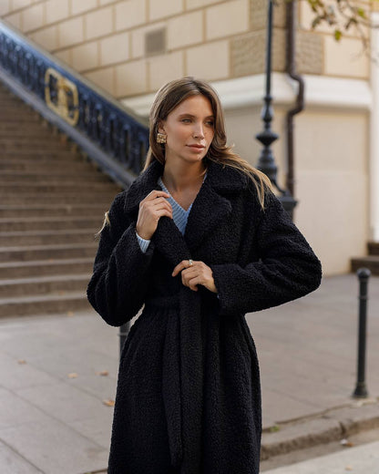 Woman wearing a black coat standing on a city street.