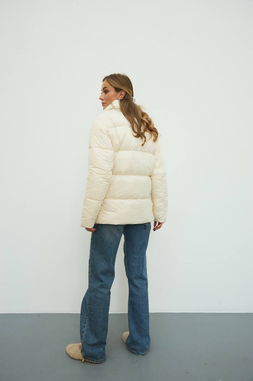 Person wearing a white puffer jacket and blue jeans against a plain background