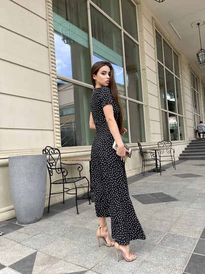 Woman in a black polka dot dress standing outside a building.