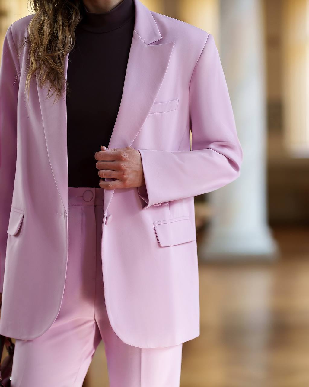 Person wearing a light pink suit with a blurred background