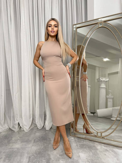 Woman in a beige dress standing in front of a large mirror in a room with white curtains.